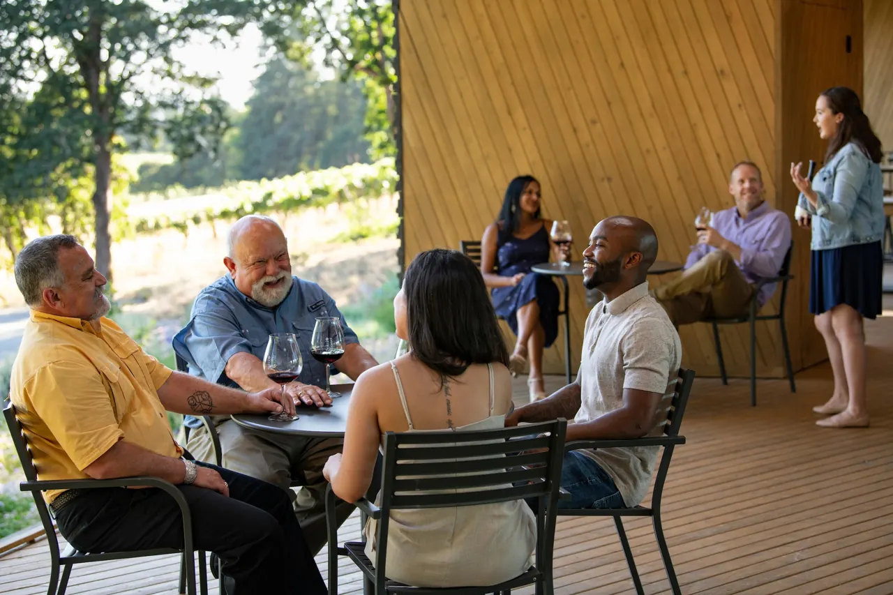Friends laughing over glasses of wine at a table on the tasting room patio