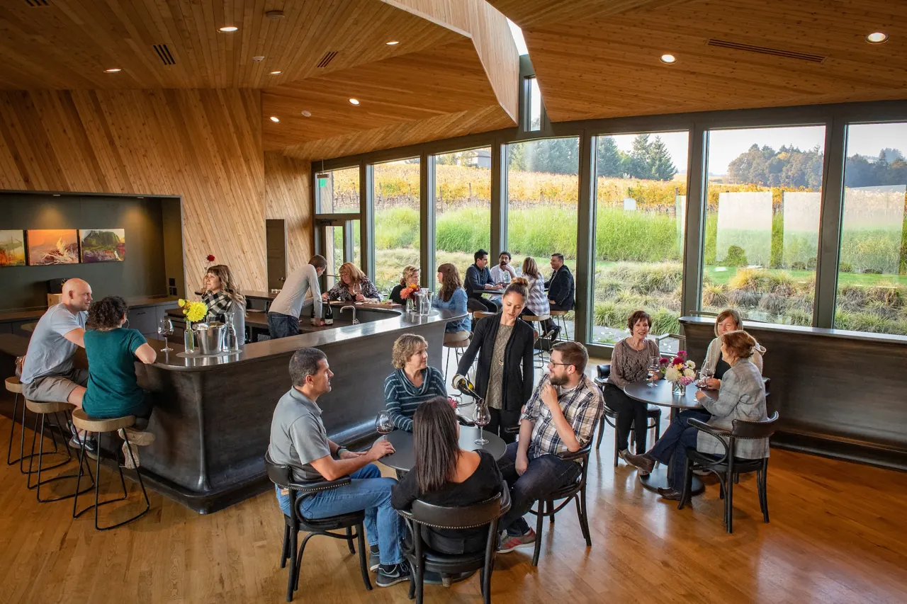 Guests at tables and the tasting bar in the bright, wood-ceilinged tasting room